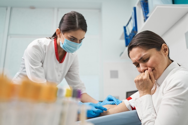 Negative emotions. Worried young woman wrinkling her forehead while making fist during sampling blood for test