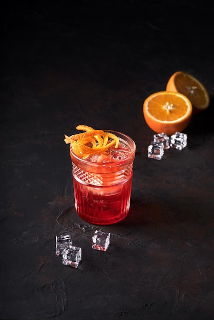 Negroni Cocktail with Orange Twist and Pin on Dark Background and next to it orange and ice Beverage Photography