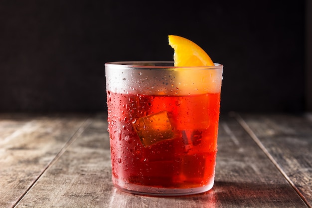 Negroni cocktail with piece of orange in glass on wooden table