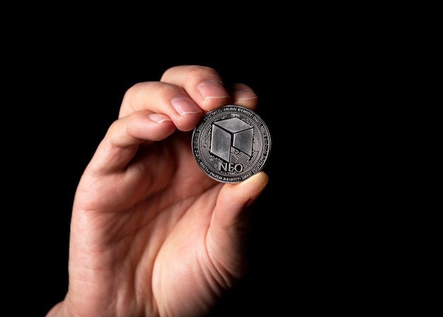 NEO shiny silver coin in male hand over black background.