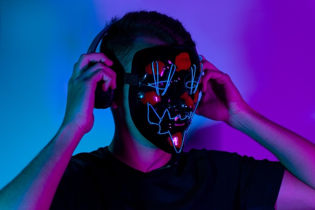 Neon portrait of man wiht mask in headphones, black t-shirt. Listening to music