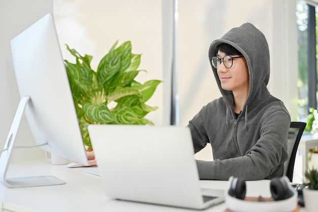 Nerd young Asian male website developer or programmer focusing on his task on computer