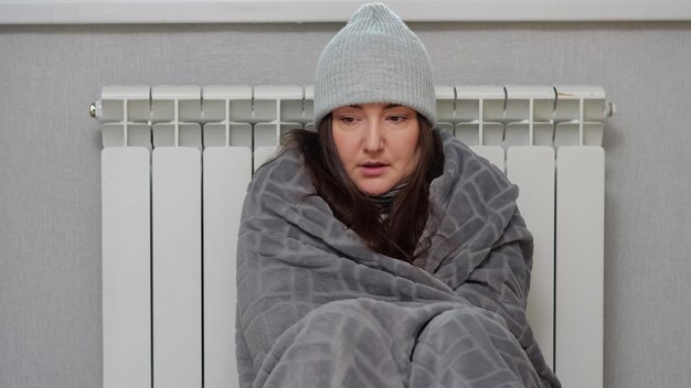 Nervous adult woman sits leaning on battery and warms up