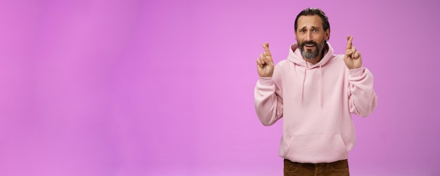 Nervous unsure hopeful handsome bearded s man in pink stylish hoodie cringing worried cross figers g