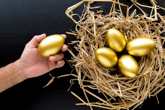 Nest Full Of Golden Eggs, Man holding a golden egg on black background. Financial success