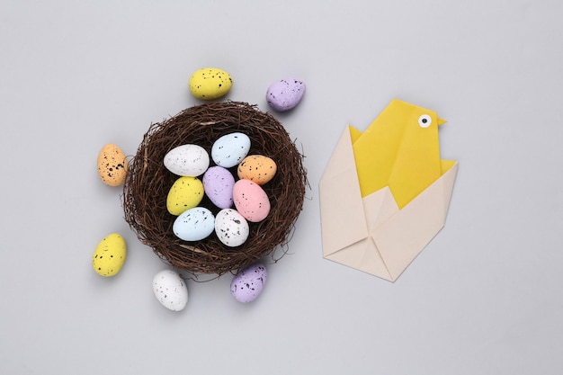 Nest with colored quail eggs and origami chicken on gray background Easter composition