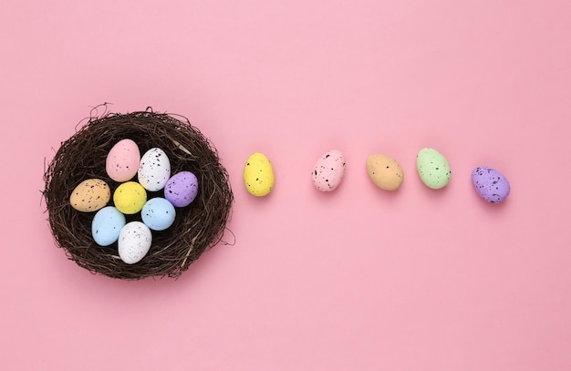 Nest with colored quail eggs on a pink background Easter composition