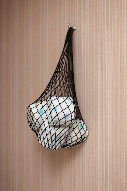 a net with toilet paper rolls hangs on the wall with a blurry background