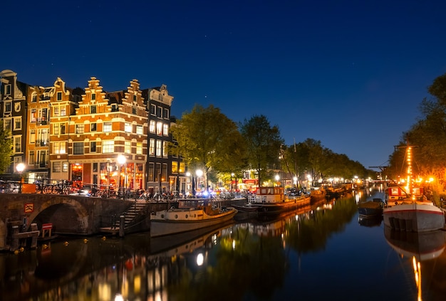 Netherlands. Calm on the night canal of Amsterdam. Residential barges and boats are moored. Reflection in the water of traditional houses and a bridge