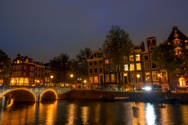 Netherlands Night on the Amsterdam canal Old stone bridge and typical houses on the embankment Traffic on the water and streets