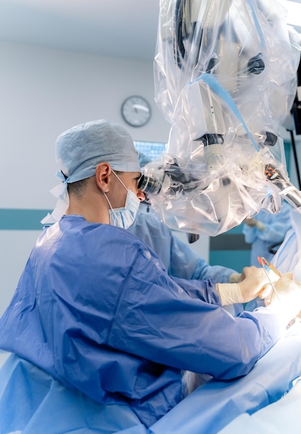 Neurosurgeon is working in operating room. Hospital background. Male doctor at work looking at surgery microscope. Hi-tech equipment.