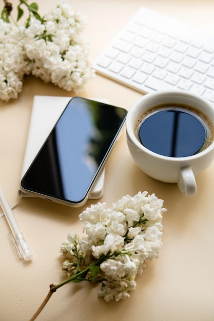 Neutral color tabletop with keyboard white lilac flowers and black smartpohone