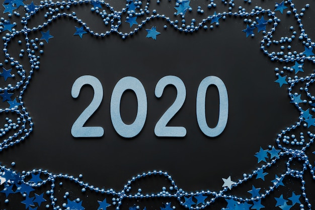 Photo new 2020 year in color classic blue. border of blue decoration, shine stars and beads on black background. happy new year. christmas party. flat lay. top view. xmas.