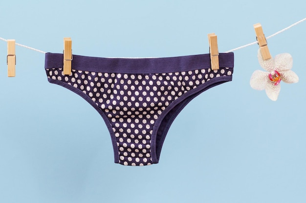 New black cotton panties on clothesline with clothespins and orchid flower in blue background. Woman underwear.