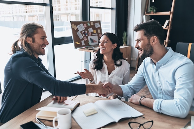 New business partners. Young modern colleagues in smart casual wear shaking hands and smiling 