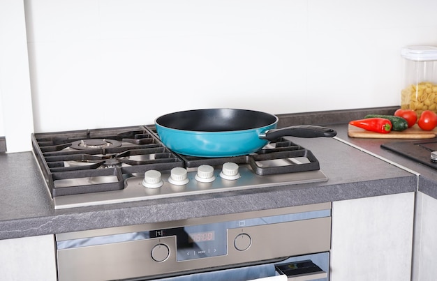 New frying pan on the stove fresh vegetables lie near the frying pan on the countertop