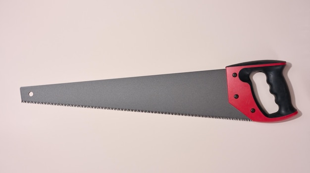 New hand saw with a rubber red handle on a beige background