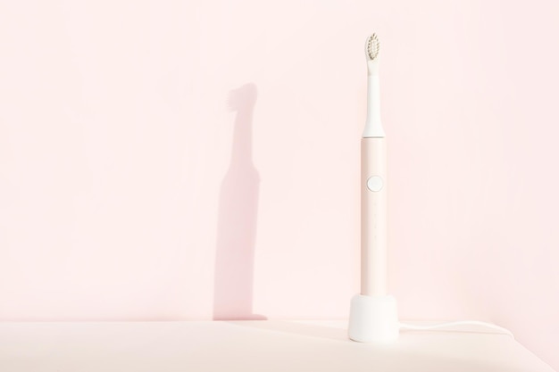 New modern ultrasonic toothbrush. Jaw model and dental care supplies on pink pastel background. Oral hygiene, dental and gum health, healthy teeth. Dental products Ultrasonic vibration toothbrush.