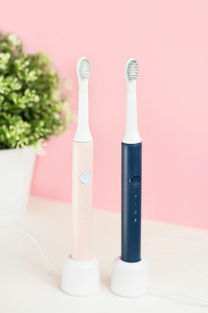 New modern ultrasonic toothbrushes. Dental care supplies with green leaves on pink pastel background. Oral hygiene, gum health, healthy teeth. Dental products Ultrasonic vibration toothbrush.