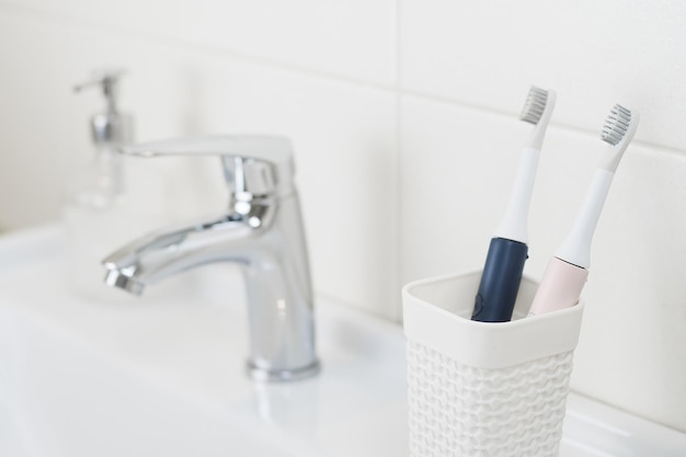 New modern ultrasonic toothbrushes in a glass on the bathroom sink. Jaw model and dental care supplies. Oral hygiene, dental and gum health, healthy teeth. Dental products.