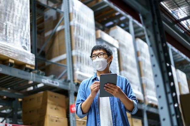 New Normal Asian men, staff, product wearing face mask. counting Warehouse Control Manager Standing, counting and inspecting products in the warehouse