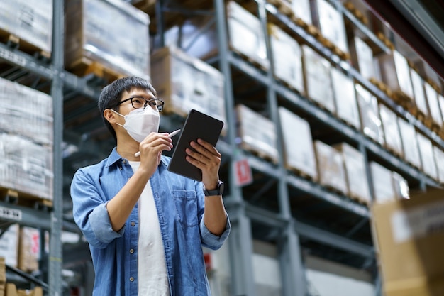 New Normal Asian men, staff, product wearing face mask. counting Warehouse Control Manager Standing, counting and inspecting products in the warehouse