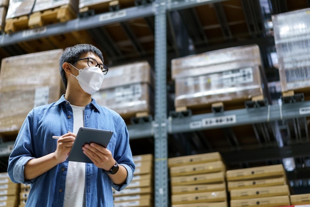 New Normal Asian men, staff, product wearing face mask. counting Warehouse Control Manager Standing, counting and inspecting products in the warehouse