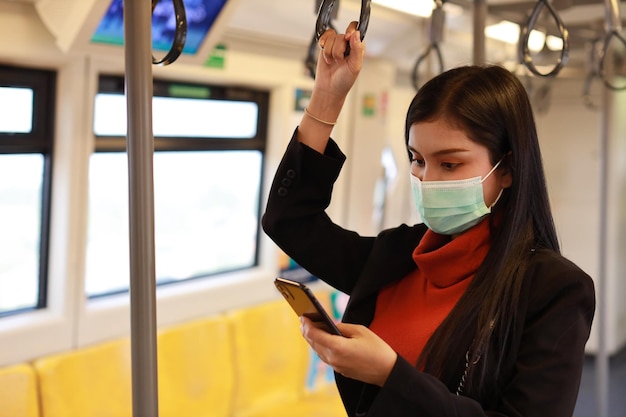 New normal covid-19 epidemic, young business asian woman wearing mask protection for prevent virus covid-19 or coronavirus infection from people in train, using smartphone communication in train