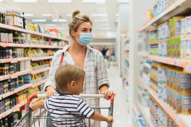 New normal in shopping. Young mother wearing prevention mask and her little son in a supermarket during virus pandemic.