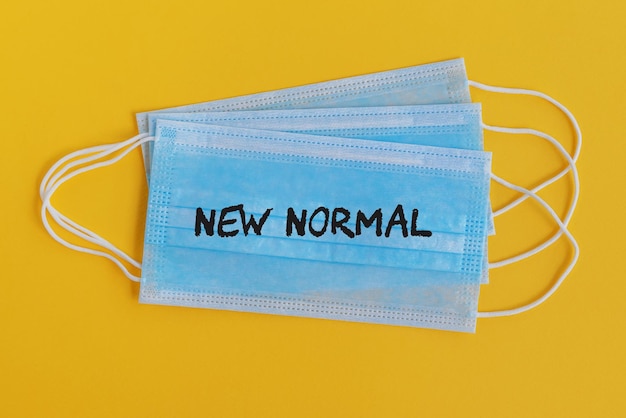 New Normal text on surgical face mask yellow background COVID19 concept