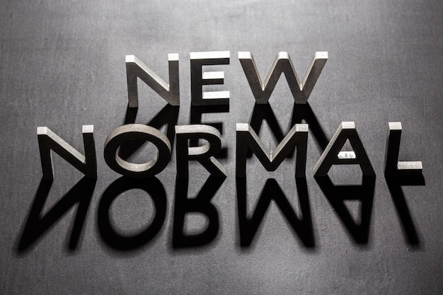 Photo new normal word composed of silver metal letters on a flat matt black surface with shadows backlit