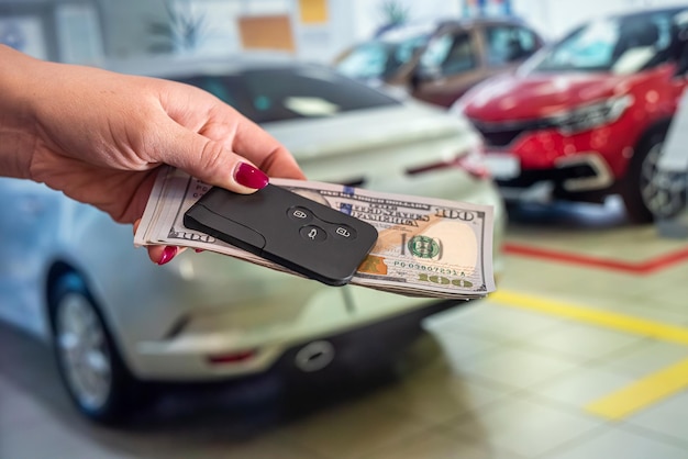 The new owner of the car holds a handful of dollars and car keys in the car showroom. The concept of buying and selling a car. Business concept