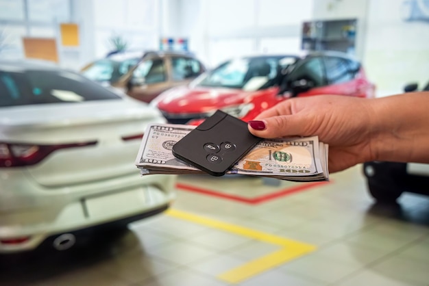 The new owner of the car holds a handful of dollars and car keys in the car showroom