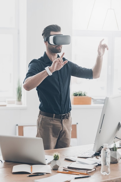 New reality is here! Handsome young man in VR headset gesturing while standing in creative office