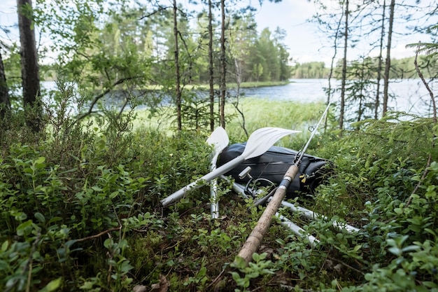 New rolled up rubber inflatable boat oars and spinning rod lie in the grass on the shore of the lake