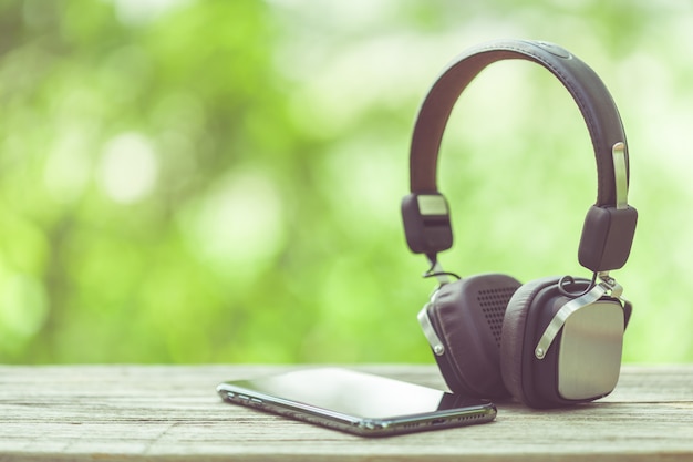 New smartphone and headphone on wooden table with green space nature blur