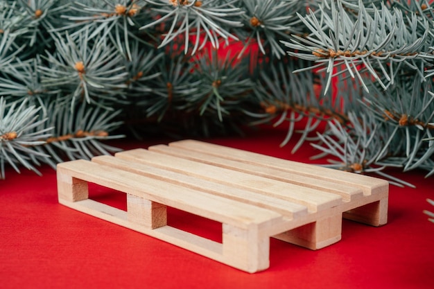 New Year 2022. Wooden pallet on red surface with Christmas tree branches. Podium, pedestal or stage. Merry Christmas.