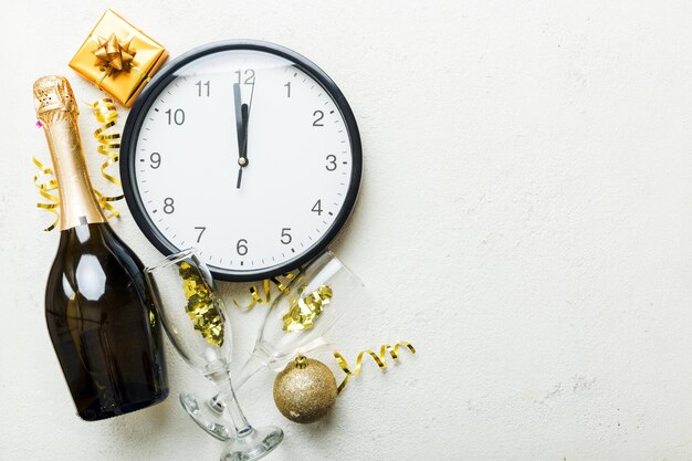 New year celebration concept with a bottle of champagne and two glasses toasting Christmas gift box alarm clock and fir tree branch on colored table Top view Copy space