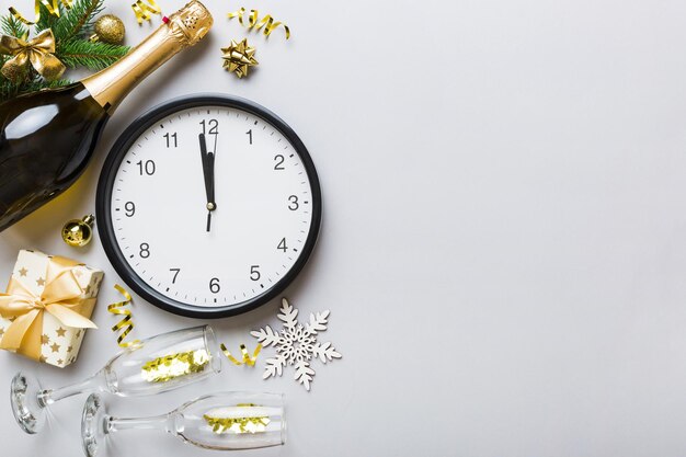 New year celebration concept with a bottle of champagne and two glasses toasting Christmas gift box alarm clock and fir tree branch on colored table Top view Copy space