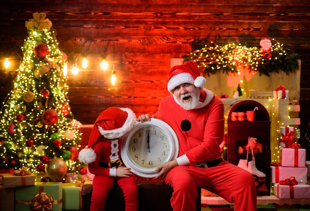 New year and christmas santa man and little assistant holds old clock kid boy dressed as santa claus