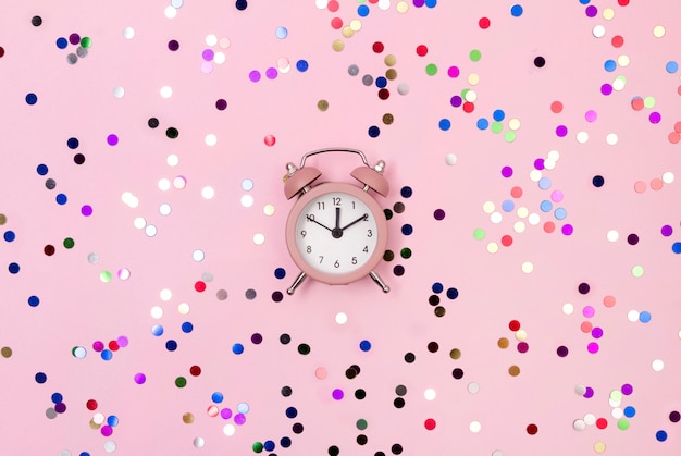 New Year Christmas top view flat lay pink alarm clock with colorful confetti copy space background