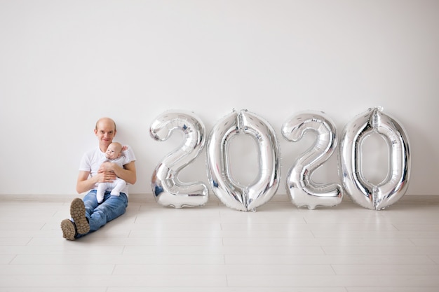 new year concept - Proud father holding his newborn baby daughter near 2020 balloons