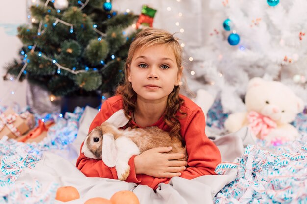 New Year a girl in a New Years sweater holds a rabbit near the Christmas tree