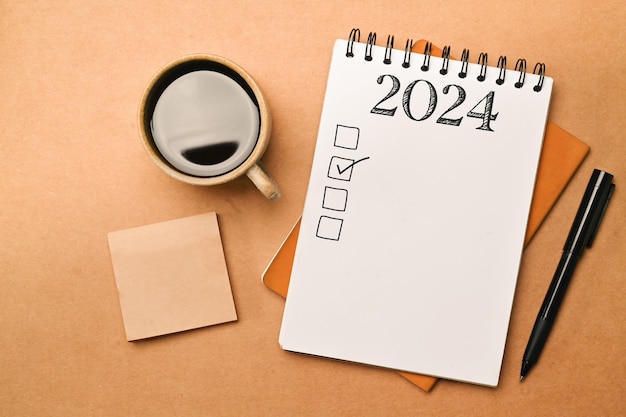 New year goals 2024 concept Notebook coffee cup and pen on brown background