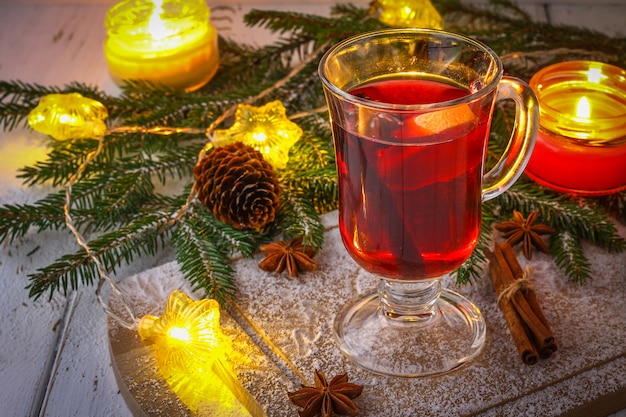 New Year mulled wine in a glass on the background of twigs, candles and garlands.