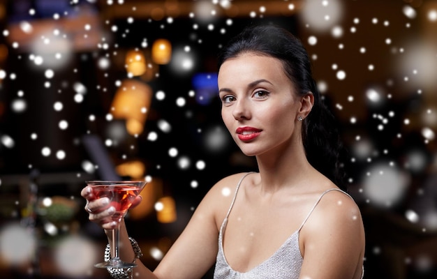 new year party, christmas, winter holidays and people concept - glamorous woman with cocktail at night club or bar over snow