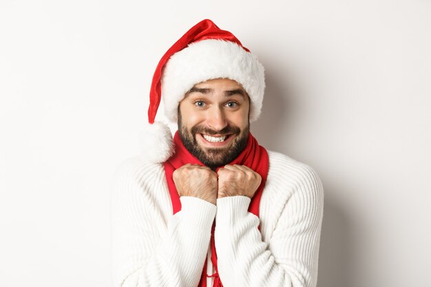 New Year party and winter holidays concept. Handsome guy in Santa hat feeling excited about Christmas, standing amused against white background