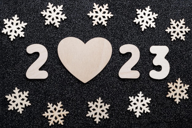 Photo new year's card 2023 wooden numbers of the year heart shape and snowflakes on a shiny black starry background