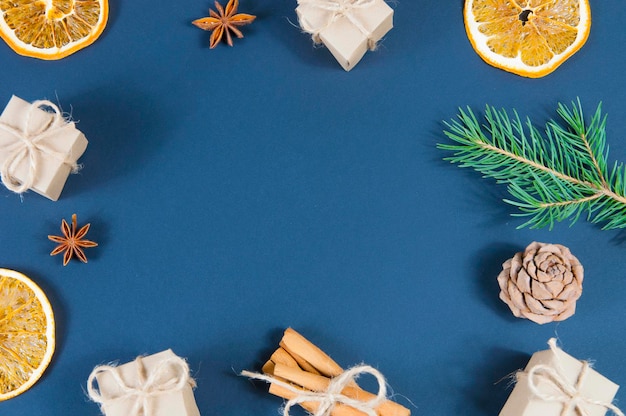 New Year's Christmas decoration frame of gift boxes, dried orange slices, green spruce branch,anise and cinnamon on a blue background top view.