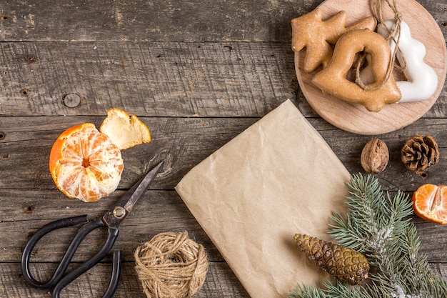 New Year's composition. Gift wrapping paper, scissors, spruce branch and Christmas gingerbread cookies on a wooden background. Christmas, winter, new year concept. Flat lay, top view.